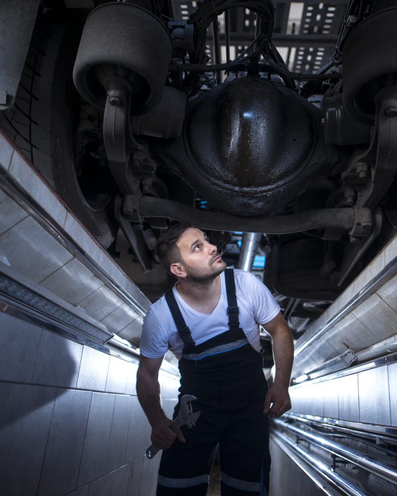 Professional mechanic serviceman under the truck looking for an oil leak in vehicle repair shop.